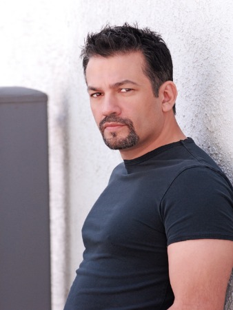 Maria Canals-Barrera's husband David Joel Barrera in black T-shirt leaning against a white wall